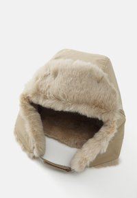 Cappello in finta pelliccia beige con un bordo morbido e soffice e un guscio esterno liscio. Include una sottile cinghia per la regolazione alla base.