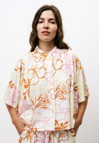 Korte mouw, knoopsluiting shirt in witte stof met bloemmotieven in oranje, roze en geel. Heeft een ontspannen pasvorm en een kraag.