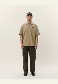 Beige polo skjorte med krage og korte ermer, kombinert med olivengrønne cargo-bukser med sidelommer og svarte sko.