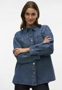 Denim overshirt in mid-blue, featuring a button-up front, two chest pockets, and a collared neckline. Relaxed fit with long sleeves.