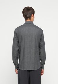 Camisa gris de manga larga con un sutil patrón de cuadros, puños abotonados y un collar clásico. Tejido ligero con una textura suave.