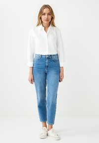 White button-up shirt with rolled sleeves paired with high-waisted blue jeans and white sneakers, featuring a straight leg cut and classic design.