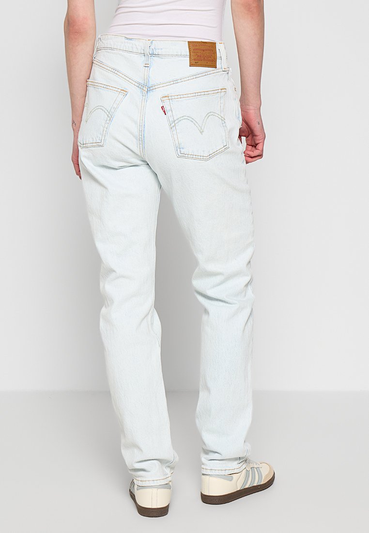 Jeans de mezclilla azul claro con un corte de pierna recta, bolsillos traseros prominentes y una etiqueta de marca de cuero marrón en la cinturilla.