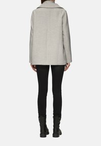 Grauer strukturierter Mantel mit breitem Kragen, taillierter Form und weicher Textur. Kombiniert mit schwarzen Slim-Fit-Hosen und Ankle-Boots.