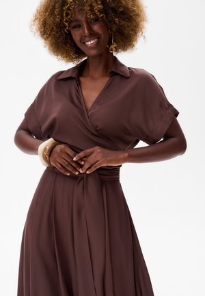 Robe en tissu marron avec des manches courtes et une taille à nouer. Tissu lisse avec un éclat subtil, dotée d'un col classique et d'une jupe fluide.