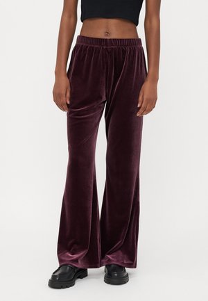 Pluche, diep bordeauxrode fluwelen wijde broek met een elastische tailleband, met een gladde textuur en een losse pasvorm, gecombineerd met zwarte chunky schoenen.
