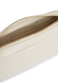 Κρεμ δερμάτινο τσαντάκι με χρυστό φερμουάρ και μπεζ εσωτερική επένδυση, με ανάγλυφο διακριτικό λογότυπο.