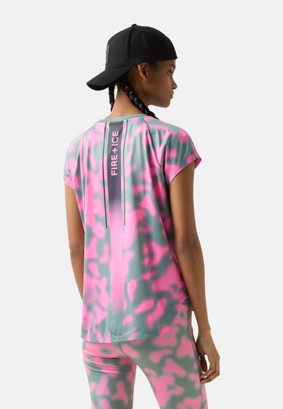 Femme aux cheveux tressés portant une casquette noire à l’envers, un haut de sport rose et gris à motifs et un legging avec le texte « FIRE + ICE » au centre du dos du haut.