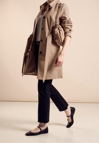 Béžový trenčkot s knoflíkovým zapínáním a ohrnutými rukávy, černé zkrácené džíny se zdobenými lemy, černé baleríny a pletená kabelka.