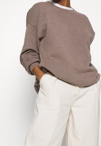 Brun sweatshirt med avslappnad passform och uppvikt ärm, parat med krämfärgade vida byxor. Mjuk textur, minimalistisk design.