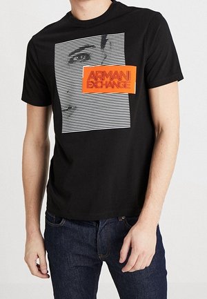 T-shirt en coton noir avec un motif graphique composé de rayures blanches horizontales et un portrait, agrémenté d'une étiquette rectangulaire orange portant la mention "ARMANI EXCHANGE".