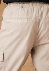 I pantaloni cargo beige presentano una vita elastica, tasche posteriori piatte e una texture liscia, adatti per un abbigliamento informale.