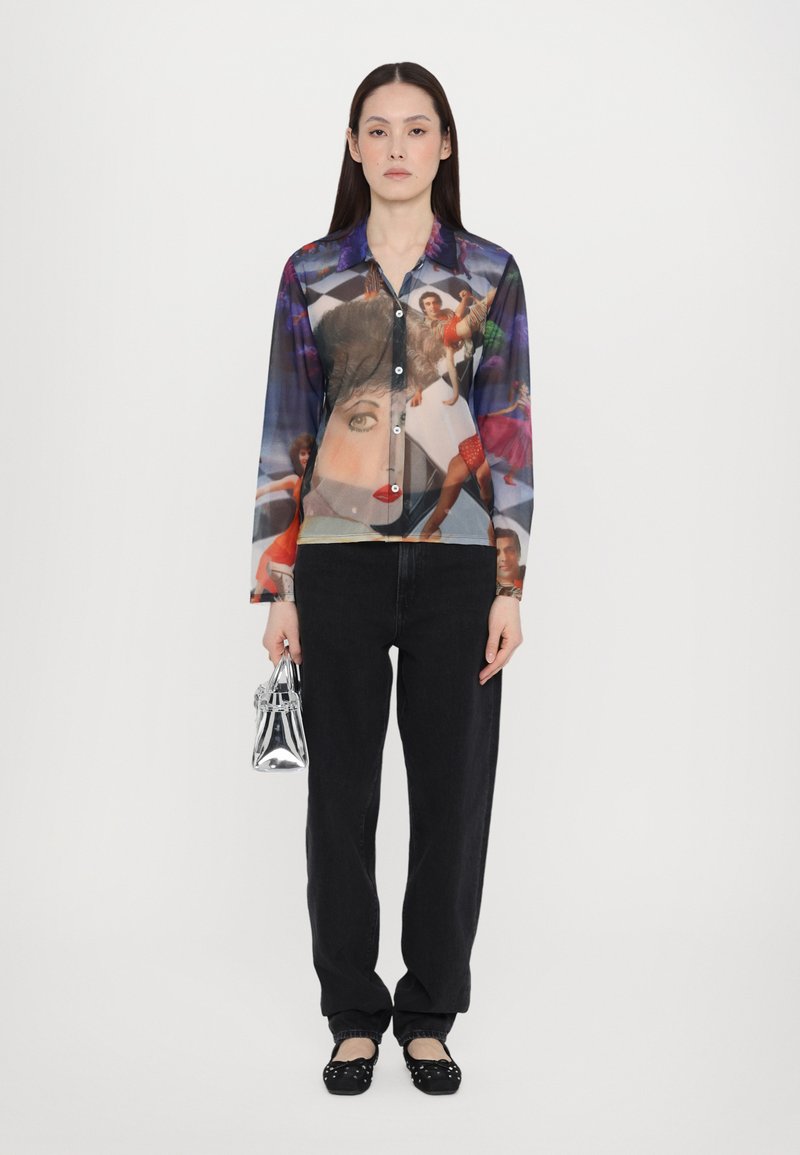 Genomskinlig skjorta med långa ärmar och knappstängning, prydd med ett färgglatt grafiskt tryck. Svarta byxor med hög midja och svarta ballerina-skor, hållandes en silverväska.