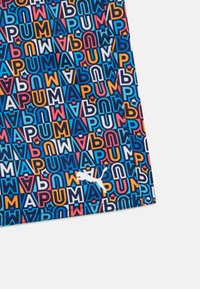Tissu de vêtements de sport coloré présentant un motif audacieux et répétitif de lettres de différentes couleurs, avec un logo Puma blanc dans le coin inférieur.