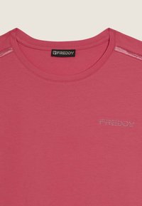 Gros plan d'un t-shirt rose à col ras du cou avec une étiquette noire "Freddy" à l'intérieur du col et le texte "FREDDY" en petits strass sur la poitrine.