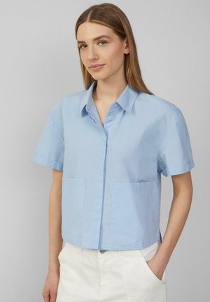 Camicetta azzurra chiara a maniche corte con colletto, due tasche frontali e una trama liscia. Fit casual e ampio.