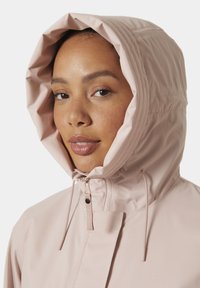 Světle růžová bunda s kapucí a hladkou texturou, která má zipové zapínání a nastavitelná šňůrky na kapuci pro pohodlné nošení.