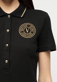 Μαύρο κοντομάνικο πόλο μπλουζάκι με χρυσά κουμπιά και κεντημένο λογότυπο Versace Jeans Couture στο αριστερό στήθος.