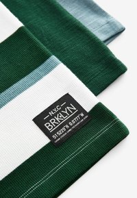 Pruhovaná látka v zelené, bílé a světle modré barvě, s texturovaným povrchem. Obsahuje černou nášivku s bílým textem.