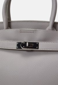 Grijze leren handtas met een gestructureerde afwerking, voorzien van een zilveren sluiting. Dubbele handgrepen en een eenvoudig ontwerp benadrukken functionaliteit.