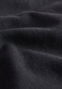 Gros plan sur un tissu noir montrant une texture tissée fine et des plis souples.