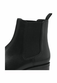 Svart läderankle boot med elastiska sidopaneler, en slät yta och en texturerad detalj. Utrustad med en liten dragflik för enkel påtagning.