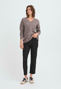 Suéter de cuello en V en marrón claro, tejido texturizado; combinado con jeans negros de cintura alta y zapatillas beige con acentos negros.