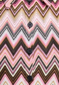 Nööpidega särk, millel on roosa, musta ja valge zigzag-muster, pruuni aktsentidega. Särk sisaldab nelja musta nööpi. Tekstuuriga kangas.