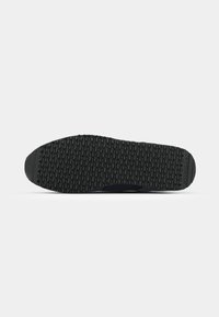 Semelle de chaussure de sport noire avec une surface texturée et un motif antidérapant. Dotée d'un bout arrondi et d'une surface plate pour une meilleure traction et stabilité.