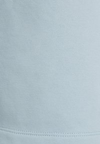 Detailní záběr na světle modrou tkaninu ukazující jemnou pletenou strukturu a horizontální dvojitý steh blízko spodního okraje.