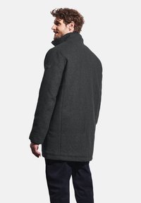 Uhlová vlněná bunda s vysokým límcem, bočními kapsami a texturovaným povrchem. Obsahuje nášivku na rameni a má rovný střih.