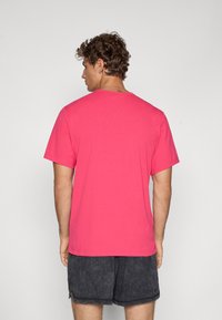 Kortærmet T-shirt i lys pink bomuld, med en klassisk rund hals og en afslappet pasform, iført mørke shorts.