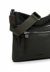 Dark green nylon crossbody bag with a textured surface, featuring a front zip pocket, brown leather accents, and a sturdy strap.
