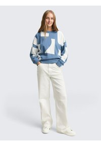 Blauw-witte geblokte sweatshirt met een ontspannen pasvorm, lange mouwen en geribbelde manchetten, gecombineerd met crème wijde broeken en witte sneakers.