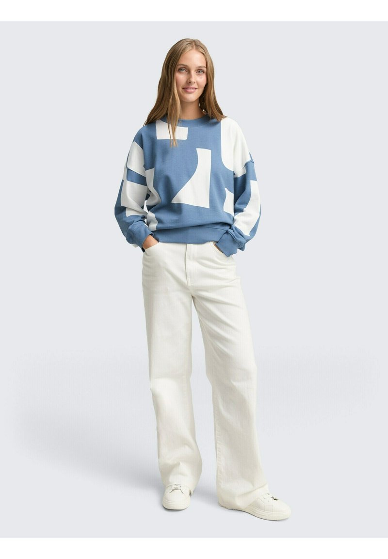 Blauw-witte geblokte sweatshirt met een ontspannen pasvorm, lange mouwen en geribbelde manchetten, gecombineerd met crème wijde broeken en witte sneakers.
