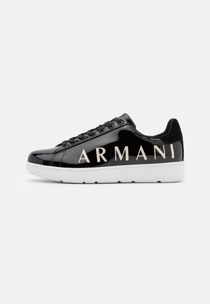 Schwarzer glänzender Sneaker mit weißer Sohle und großem "ARMANI" Text an der Seite, von der Außenseite auf einem schlichten hellen Hintergrund gezeigt.