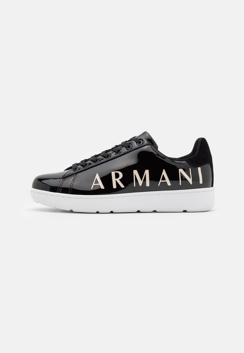 Baskets noires brillantes avec une semelle blanche et un grand texte "ARMANI" sur le côté, vues de l'extérieur sur un fond clair uni.