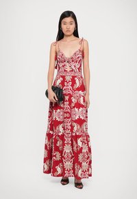 Maxi dress in red with white floral and paisley patterns. Features a deep neckline, adjustable straps, and a tiered skirt design.