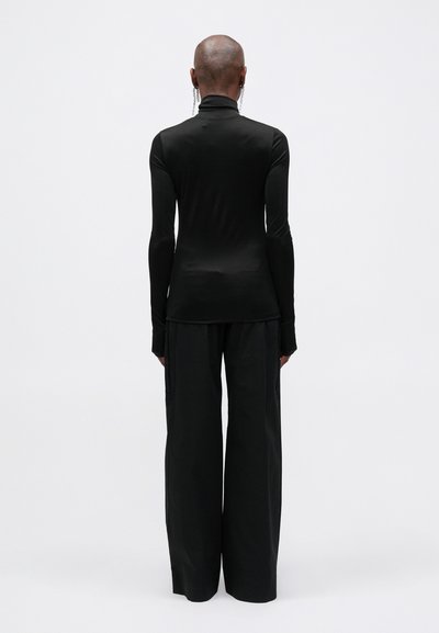 Cămașă neagră cu mâneci lungi și gulere înalt, asortată cu pantaloni negri evazați. Textură netedă și design minimalist, fără modele vizibile.