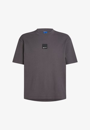 Siva kratka majica s kratkimi rokavi iz teksturirane rebraste tkanine, okrogel izrez in črno kvadratno nalepko na sprednjem delu. Mehka, sproščena kroja.