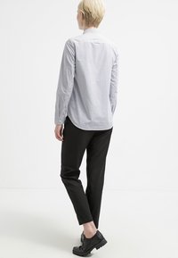 Chemise à rayures boutonnée en bleu clair et blanc, associée à un pantalon noir ajusté et des chaussures noires. La chemise présente un ourlet arrondi et des manches longues.