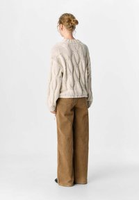 Chunky beige stickad tröja med ett texturerat snårmönster, tillsammans med vida bruna manchesterbyxor. Neutral färgpalett, avslappnad passform.