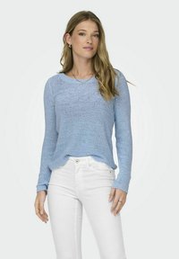 Pull en tricot bleu clair avec un col rond et des manches longues, présentant des poignets côtelés et une coupe décontractée, associé à un jean blanc.