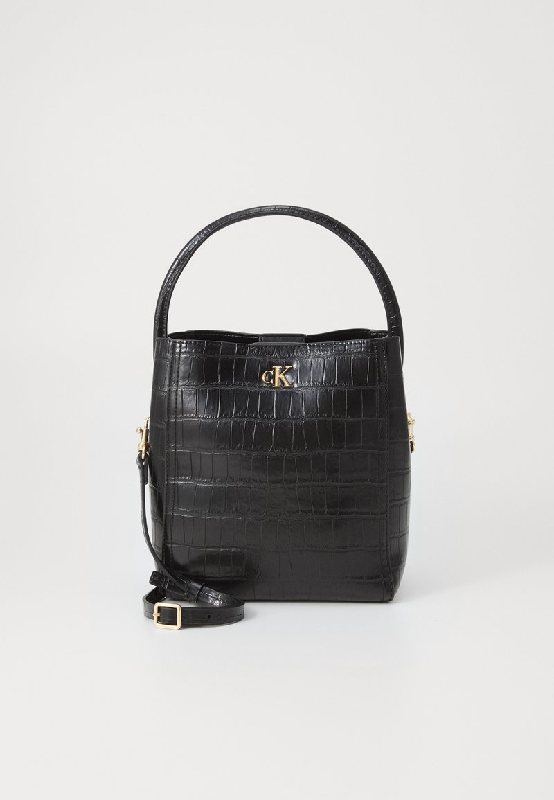 Sac à main noir en cuir synthétique façon crocodile, avec poignée supérieure, bandoulière amovible et petit logo doré "cK" à l'avant.