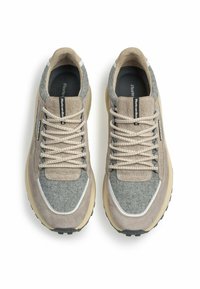 Sneaker beige e grigi realizzati in materiale sintetico con una finitura testurizzata, dotati di lacci arrotondati e suola in gomma spessa.