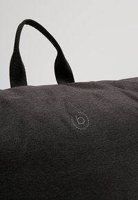 Borsa nera in tessuto con manici a doppia texture, caratterizzata da un logo in rilievo discreto. Design compatto e rettangolare con superficie liscia.