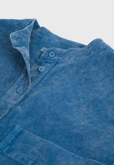 Camicia blu con bottoni, caratterizzata da un tessuto testurizzato, colletto stretto e tre bottoni allo scollo. Materiale morbido e leggero.
