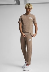 Brunt bomulds t-shirt med korte ærmer og et hvidt logo, parret med matchende joggers med logodetaljer, båret med hvide sneakers.