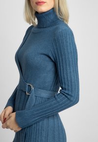 Robe en tricot côtelé bleu avec un col montant haut et des manches longues, dotée d'une taille ceinturée et d'une coupe droite. Texture lisse, sans motifs.