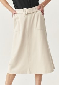 Gonna midi beige con vita arricciata, ampia cintura e grandi tasche frontali. Il tessuto appare liscio con una silhouette strutturata.